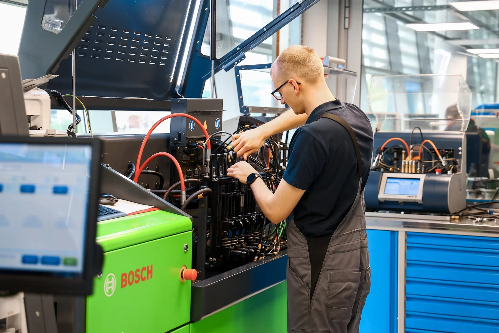 Technik wykonuje czynności przy specjalistycznym urządzeniu wyposażonym w przewody, układ pomiarowy i panel sterowania.