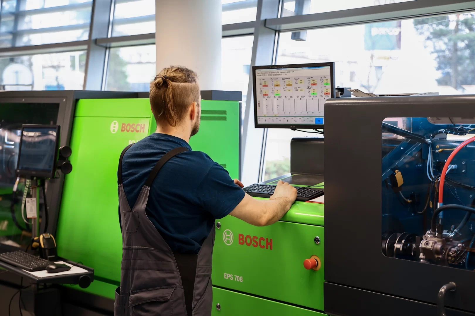 Obsługa stanowiska diagnostycznego Bosch EPS 708 Pracownik stojący przed zielonym urządzeniem Bosch EPS 708 i obsługujący komputer z monitorem