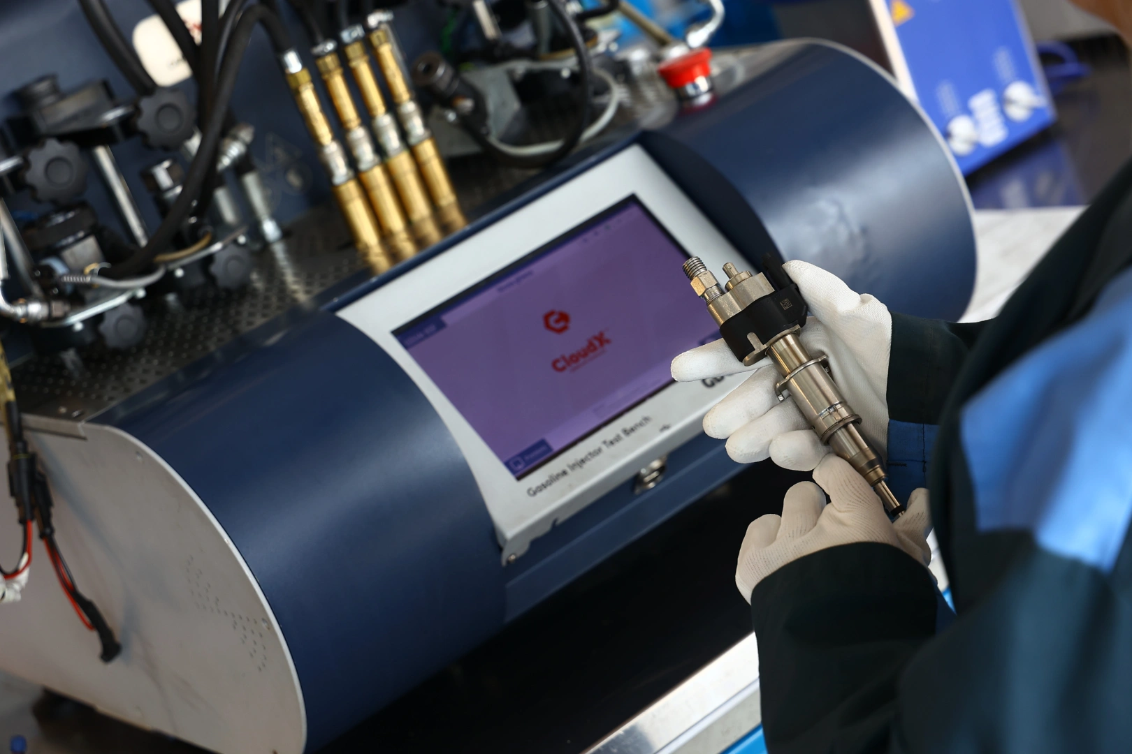 Technik w rękawicach trzymający metalowy wtryskiwacz przy urządzeniu diagnostycznym