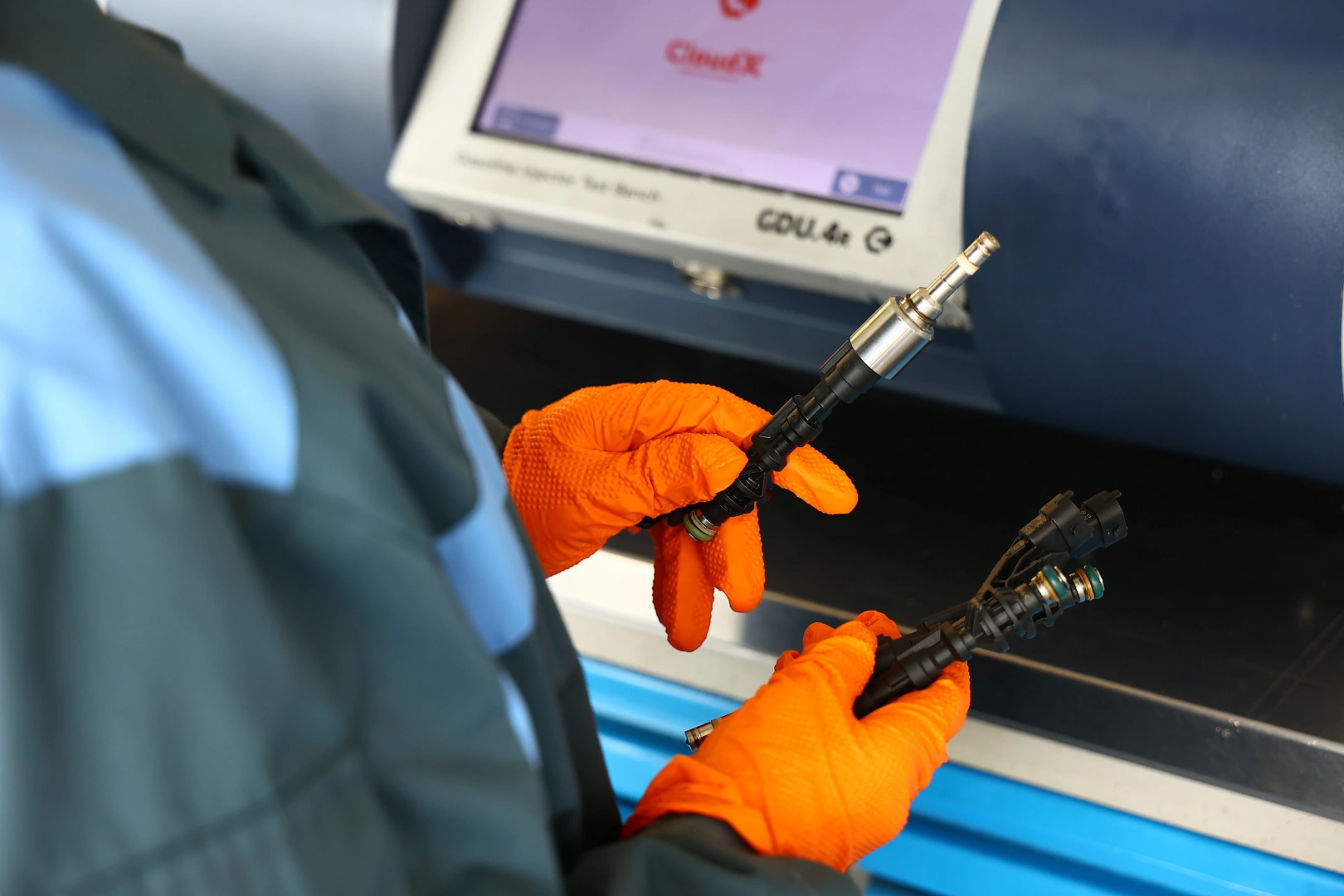 Kontrola wtryskiwaczy przed badaniem na stanowisku probierczym Technik w pomarańczowych rękawicach porównujący dwa wtryskiwacze przy urządzeniu Carbon Zapp GDU.4R