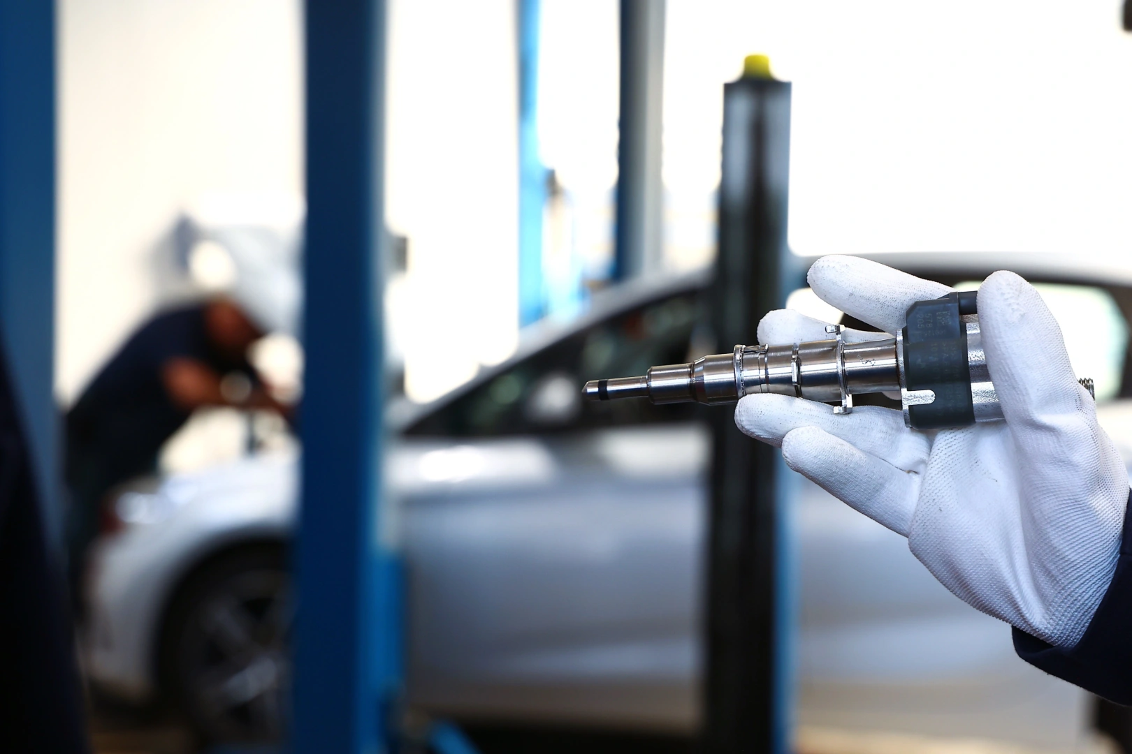 Mechanik trzymający wtryskiwacz paliwa podczas kontroli w warsztacie samochodowym Mechanik trzymający wtryskiwacz paliwa podczas kontroli w warsztacie samochodowym