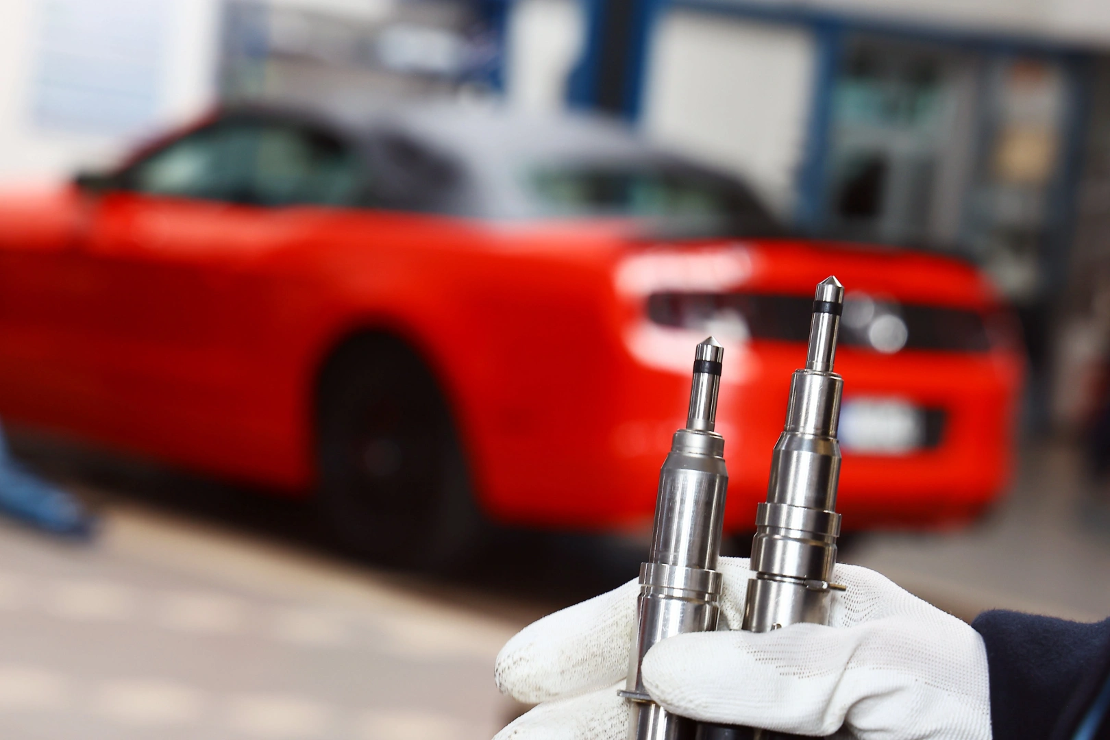 Regeneracja wtryskiwaczy benzynowych w profesjonalnym warsztacie Regenerowane wtryskiwacze benzynowe trzymane przez mechanika na tle samochodu w warsztacie