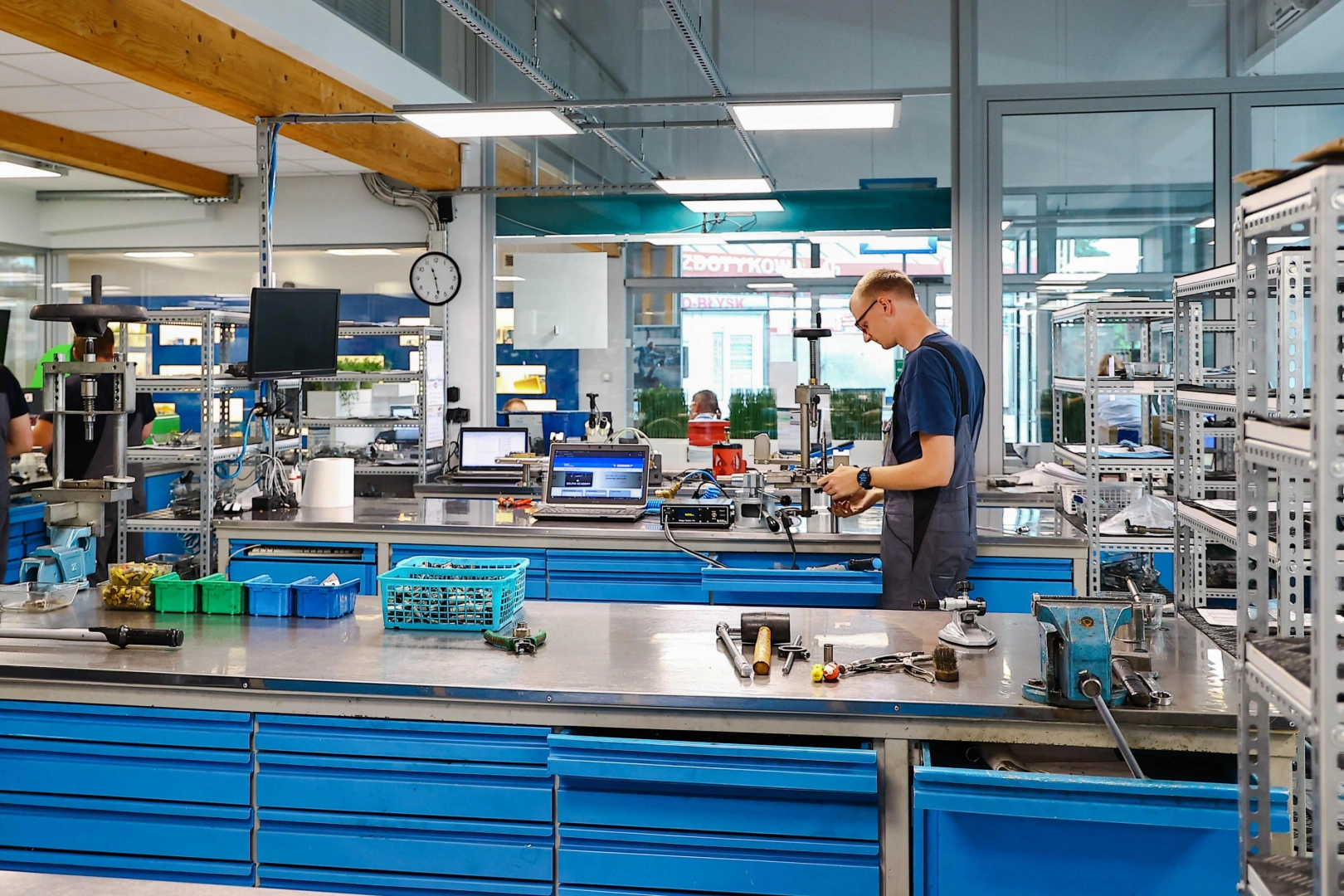 title alt Legenda obrazka Technik pracujący przy wyposażonym stanowisku warsztatowym z urządzeniami pomiarowymi i narzędziami