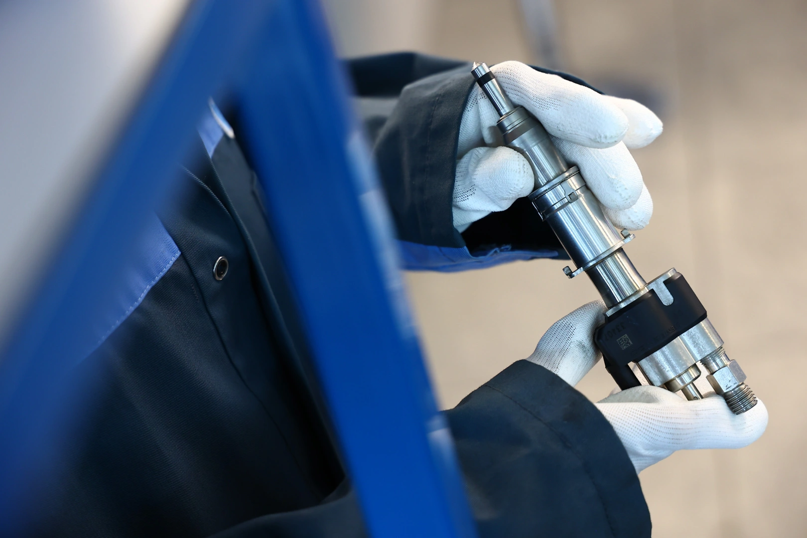 Technik trzyma metalowy wtryskiwacz benzynowy, prezentując jego konstrukcję. Technik trzyma metalowy wtryskiwacz benzynowy, prezentując jego konstrukcję.