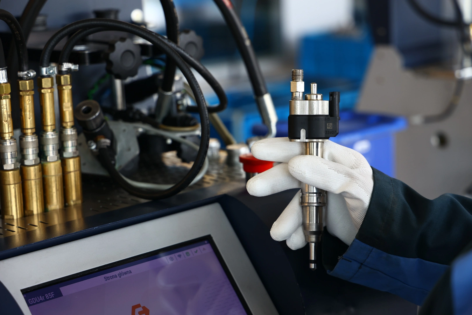 Technik trzyma wtryskiwacz paliwa przy stanowisku diagnostycznym podczas kontroli jego parametrów. Technik trzyma wtryskiwacz paliwa przy stanowisku diagnostycznym podczas kontroli jego parametrów.