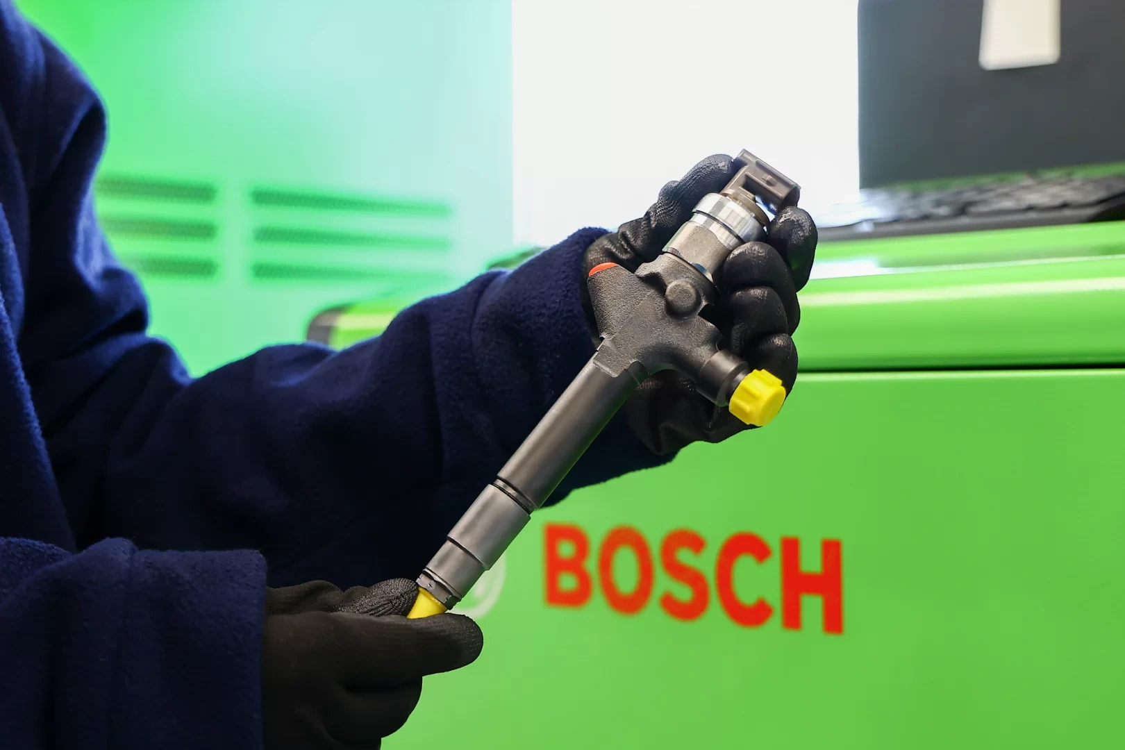 Wtryskiwacz Common Rail podczas kontroli technicznej Wtryskiwacz Common Rail trzymany w rękawicach ochronnych na tle urządzenia Bosch