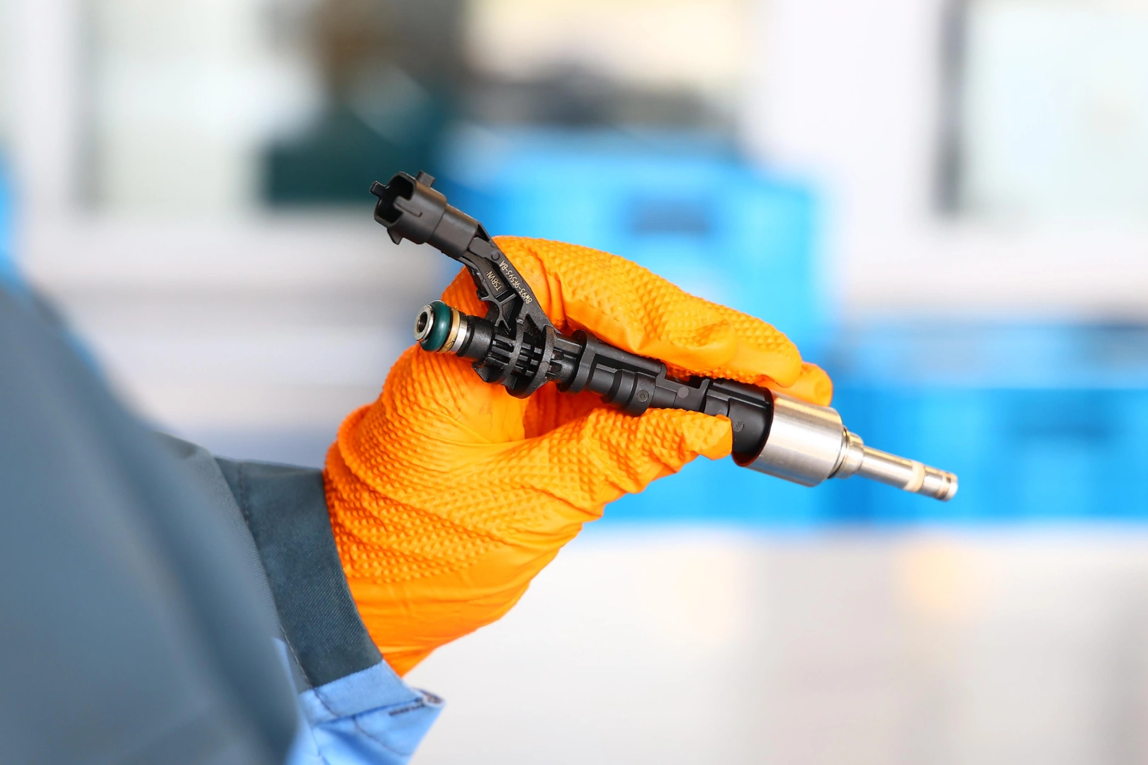 Wtryskiwacz podczas oględzin przed testowaniem Technik w pomarańczowej rękawicy trzymający metalowo-plastikowy wtryskiwacz