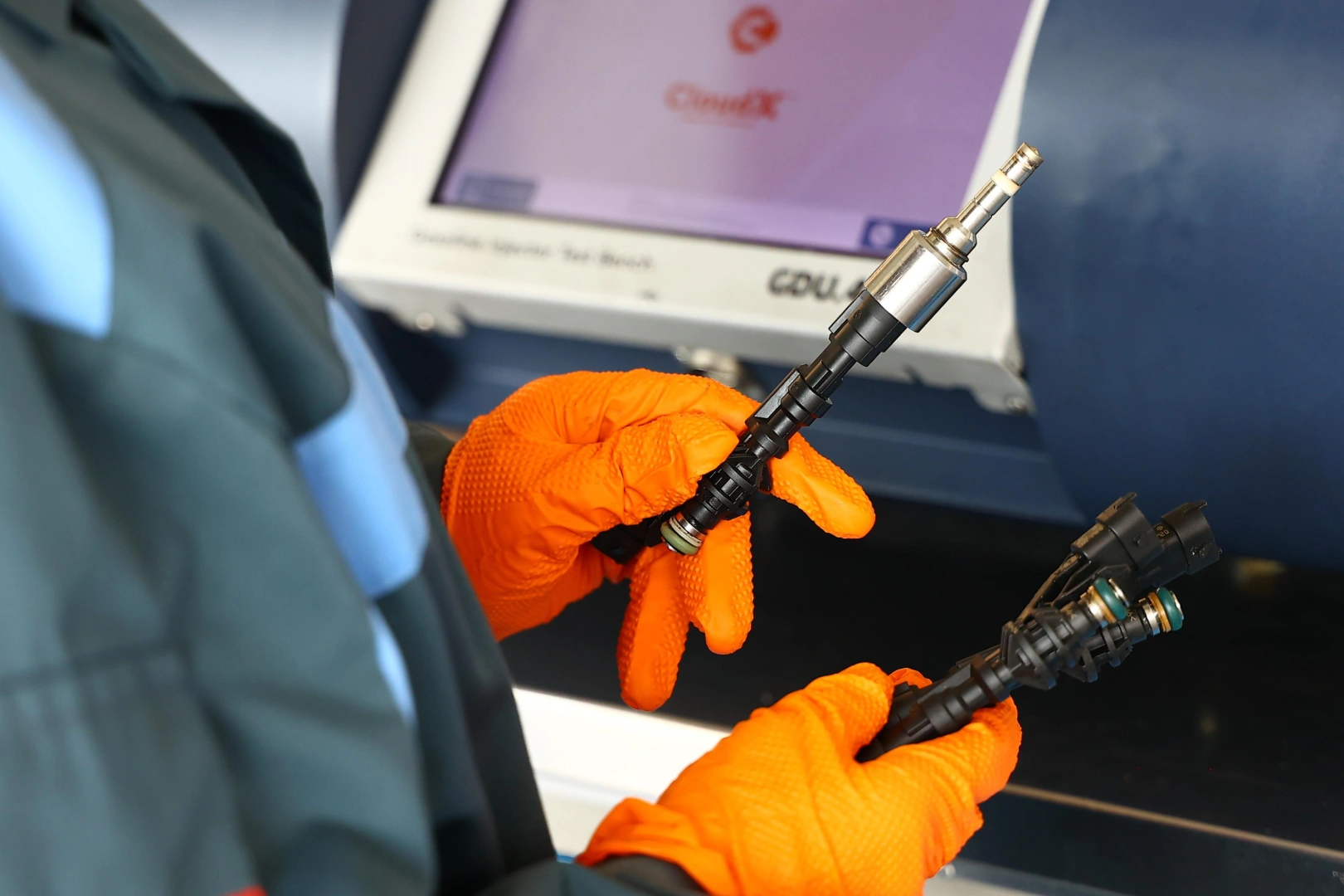 Technik w pomarańczowych rękawicach porównujący wtryskiwacze benzynowe przy stanowisku diagnostycznym