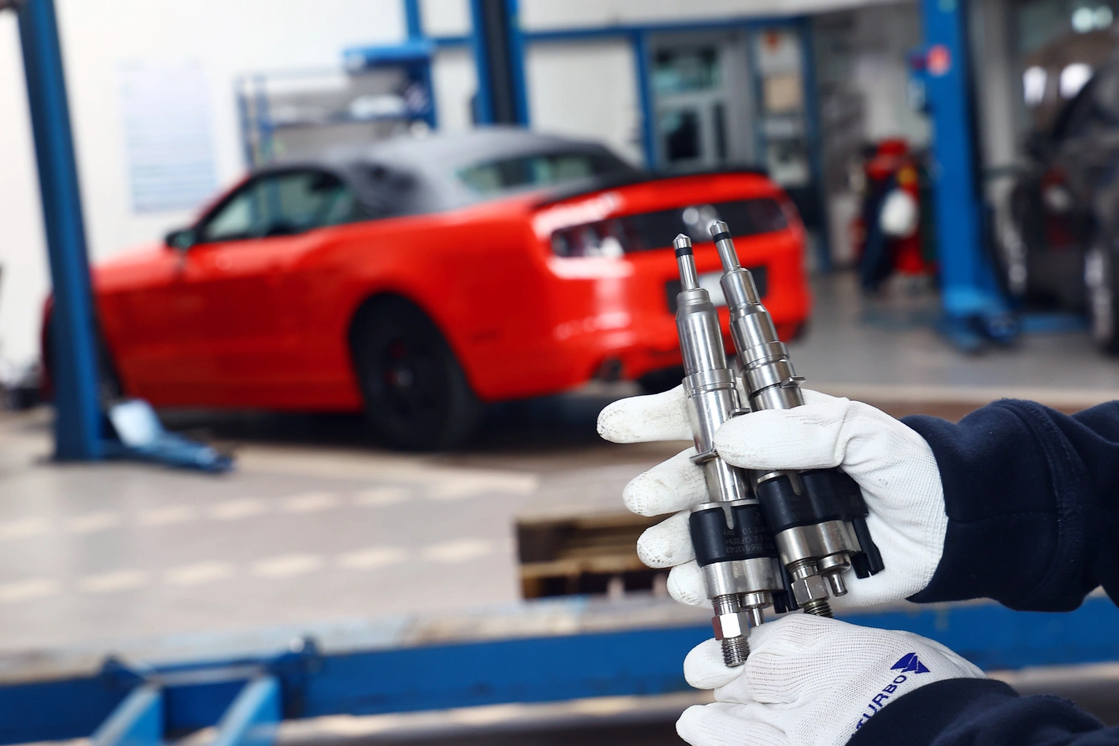 Technik trzymający dwa wtryskiwacze benzynowe na tle stanowiska serwisowego