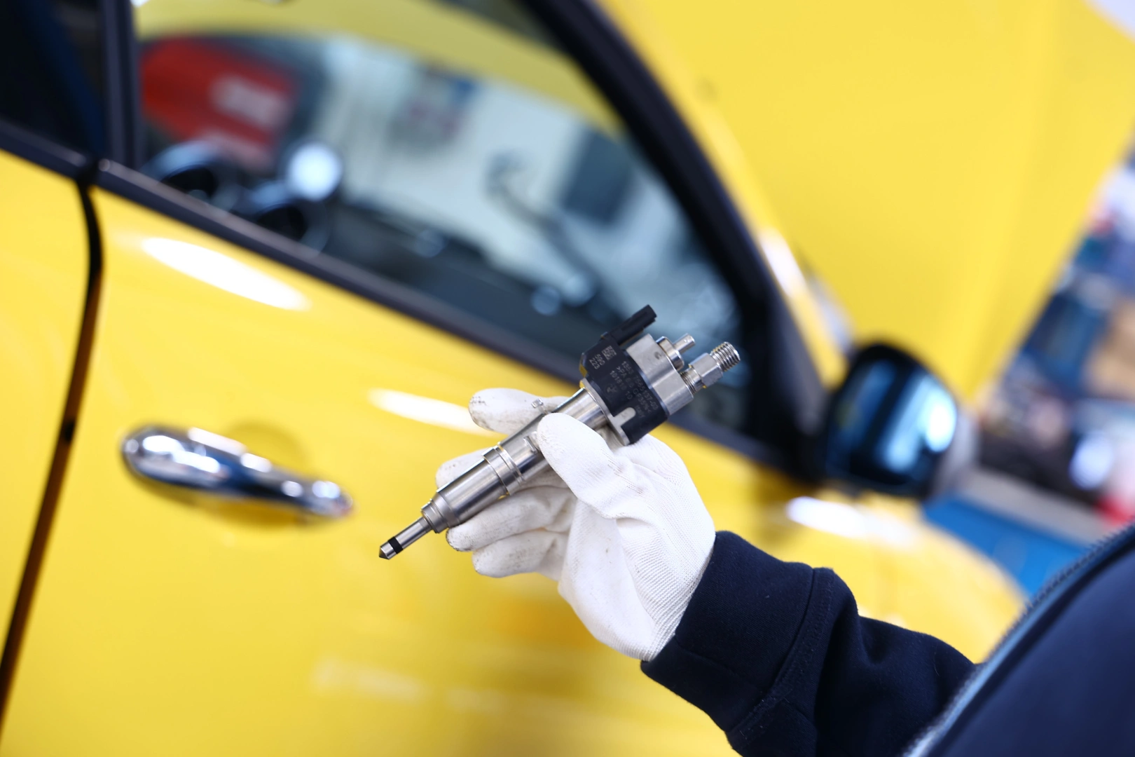 Mechanik trzymający w dłoni benzynowy wtryskiwacz paliwa przy żółtym samochodzie.